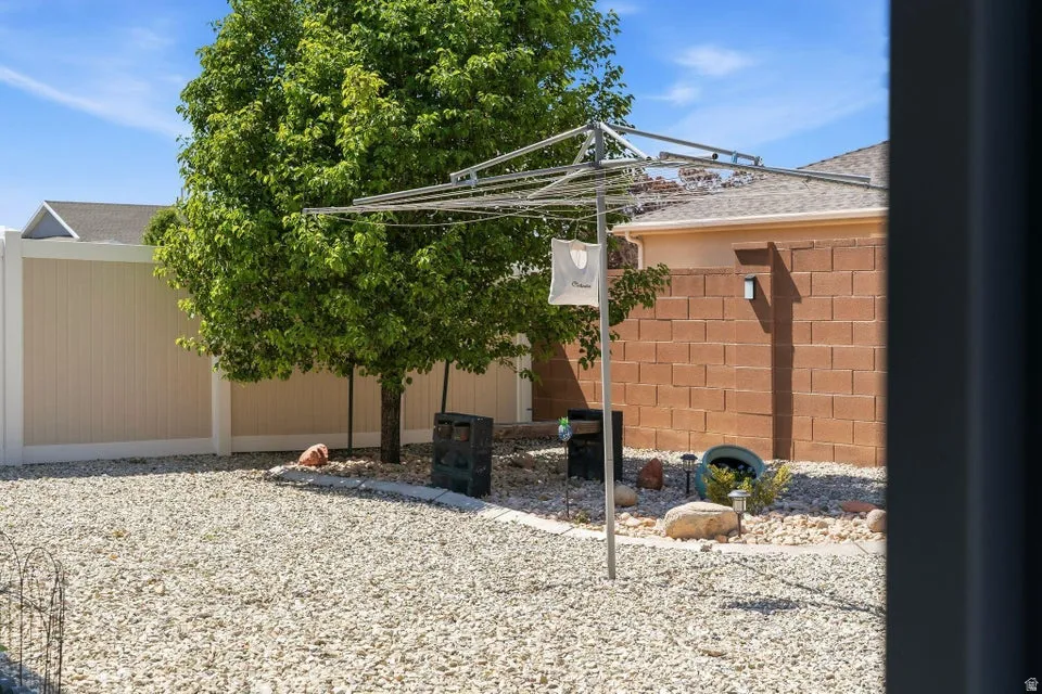Drought-tolerant gravel landscaping featuring a mature tree, privacy fencing, and an adjacent block wall structure