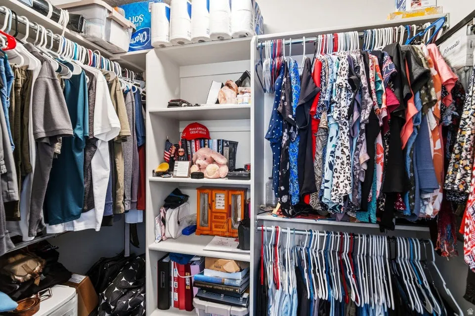 Walk-in closet featuring white shelving units, multiple clothing rods, and built-in storage