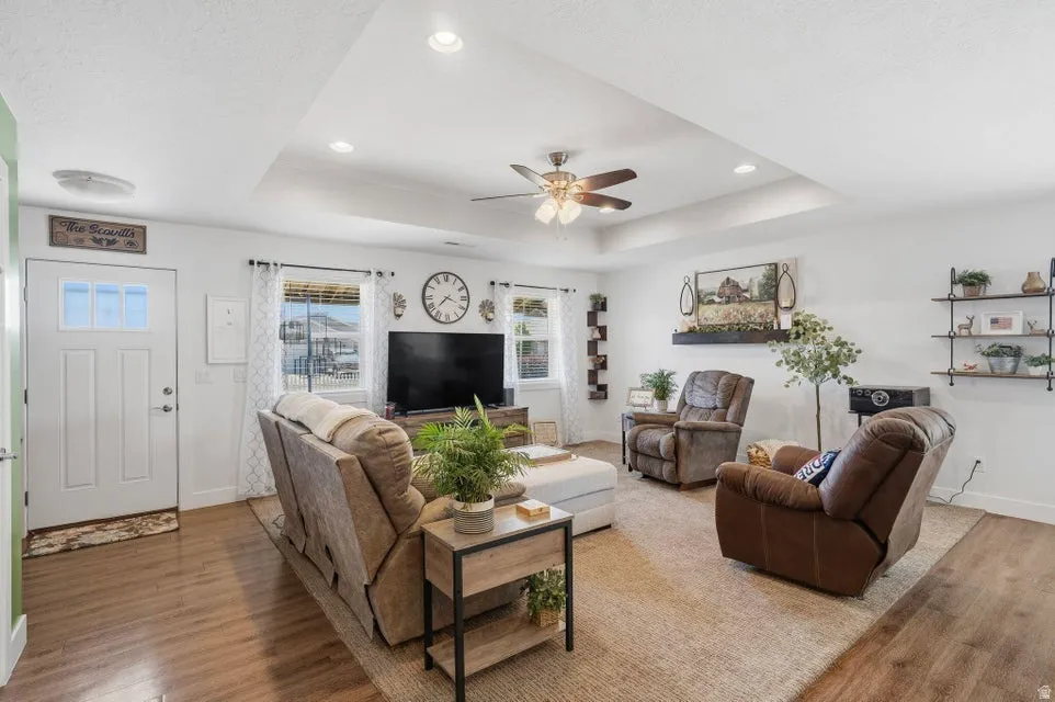 Spacious living area featuring a tray ceiling with a ceiling fan, recessed lighting, wood-finish flooring, and a decorative front entry door with transom windows
