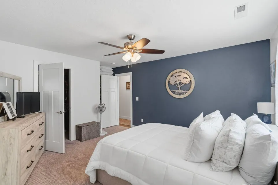 Carpeted bedroom featuring a dark accent wall, white trim, a ceiling fan with integrated lighting, and two panel doors