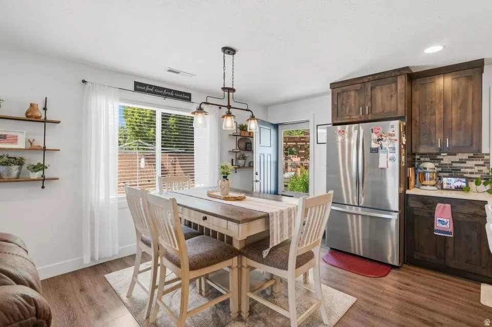 Kitchen and dining area featuring wood-finish flooring, dark wood cabinetry, a mosaic tile backsplash, and a stainless steel refrigerator