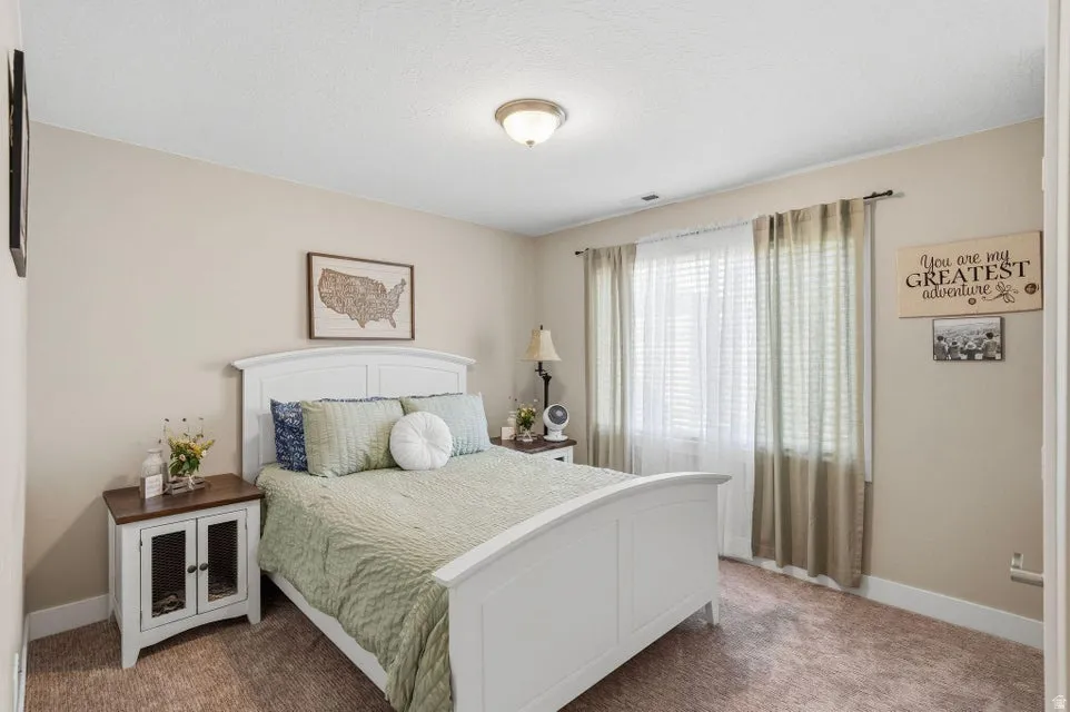 Carpeted bedroom with neutral wall tones and a window featuring blinds and drapes