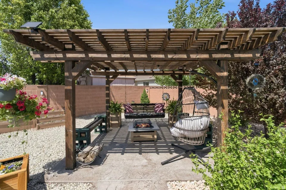 Wood pergola with integrated solar lighting system over a stamped concrete patio, featuring a built-in fire pit, surrounded by gravel landscaping, and a privacy wall