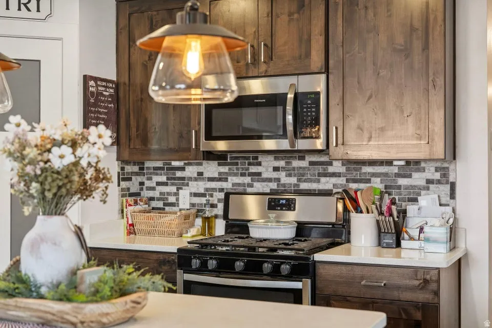 Kitchen featuring dark wood-finish cabinetry, stainless steel microwave, gas range, mosaic tile backsplash, and light countertops