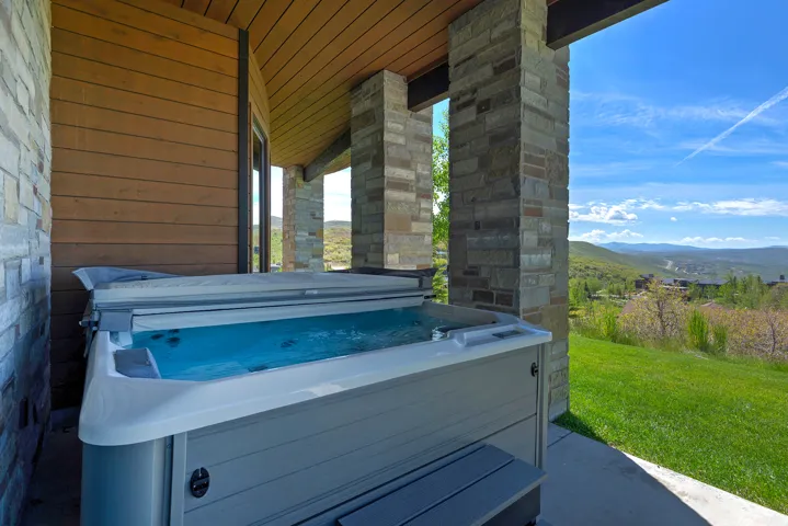 Covered patio featuring a built-in spa, stone columns, wood-paneled ceiling, and a concrete patio surface