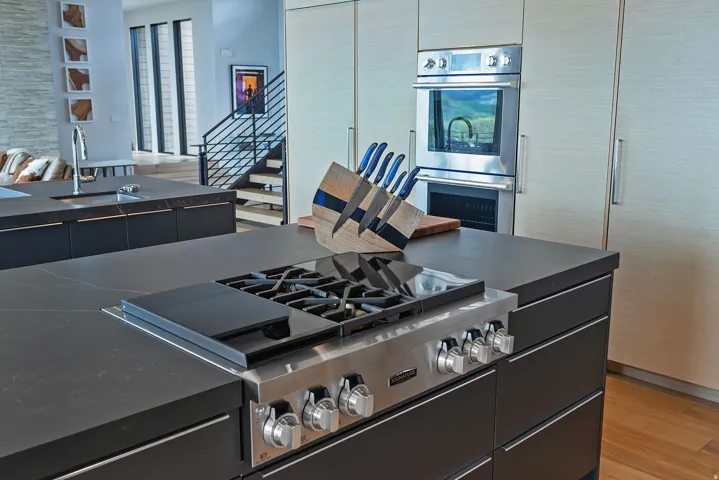 Gourmet kitchen featuring a built-in stainless steel range, double wall ovens, dark stone countertops, custom cabinetry, and wood-finish flooring
