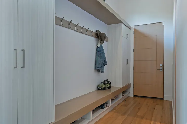 Entryway featuring built-in cabinetry, integrated bench seating, wall-mounted coat hooks, and wood-finish flooring