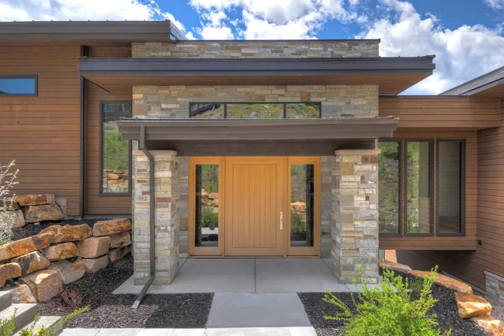 Contemporary exterior featuring a natural wood-finish door, stone accents, horizontal wood siding, and large windows