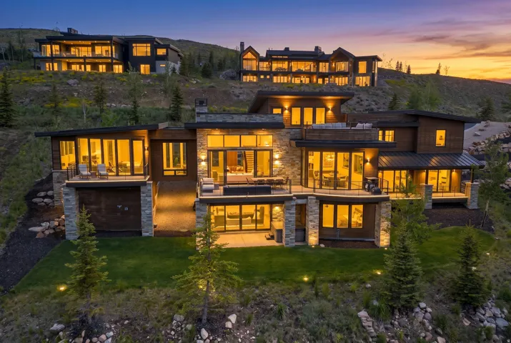 Modern architectural residence featuring multiple levels of outdoor living spaces, expansive window walls, stone accents, and a tiered landscaped yard