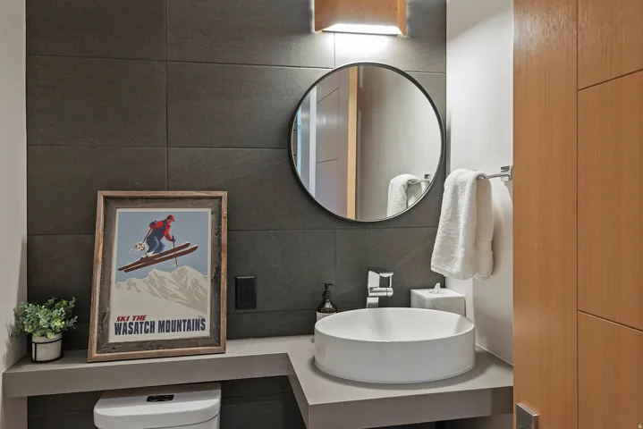 Contemporary bathroom featuring a circular vessel sink, wall-mounted faucet, and a round frameless mirror