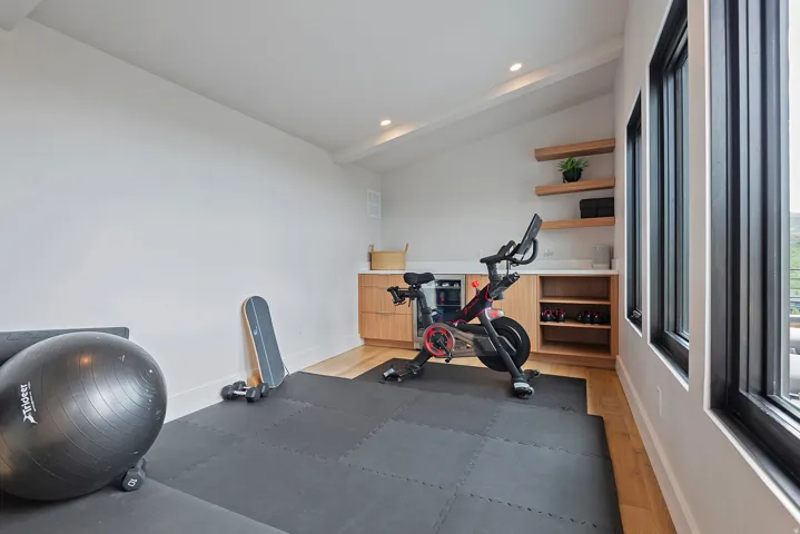 Dedicated fitness space featuring light wood-finish flooring, built-in cabinetry with a light-toned countertop, and recessed lighting