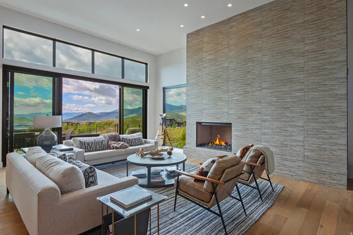 Spacious living area featuring large format sliding glass doors, upper transom windows, a floor-to-ceiling textured tile fireplace, recessed lighting, and wood-finish flooring