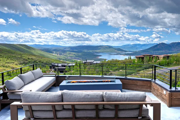 Expansive outdoor terrace featuring a built-in fire pit, metal railings, and wood-finish accent walls