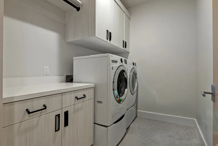 Laundry area featuring light wood-finish cabinetry, white countertops, built-in upper storage, a black hanging rod, and hex-patterned floor tiling