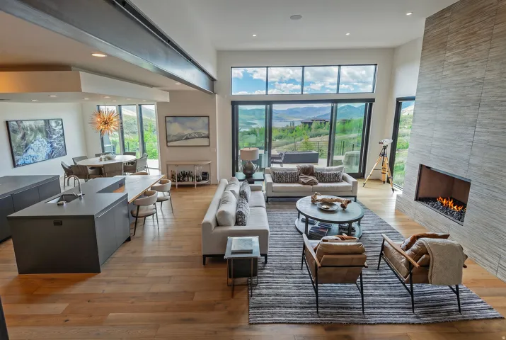 Spacious living area featuring expansive floor-to-ceiling windows, wood-finish flooring, a contemporary fireplace with a stone surround, and an open-concept kitchen island with seating