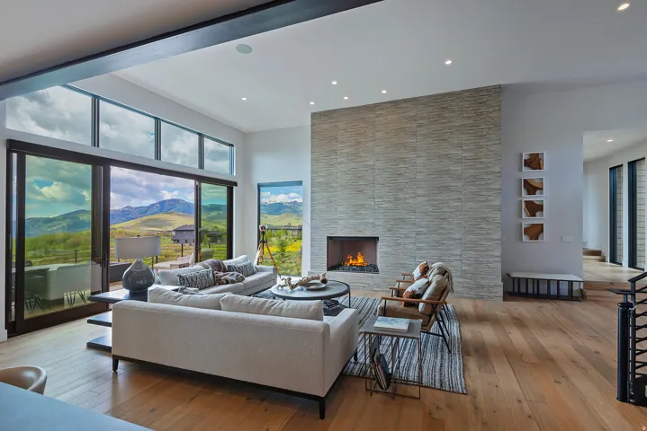 Contemporary living area featuring a floor-to-ceiling stacked stone fireplace with a gas insert, wide plank wood flooring, and extensive sliding glass doors