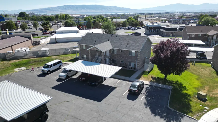 Brick exterior apartment building with covered parking, mature landscaping, and an asphalt parking lot