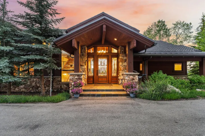 Stone and wood-clad exterior with a covered entry, featuring a wood front door with sidelight windows, and stone columns