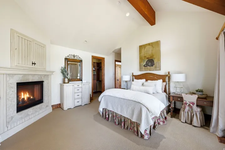 Carpeted room featuring a tiled fireplace with mantel, vaulted ceiling with exposed wood beams, and recessed lighting