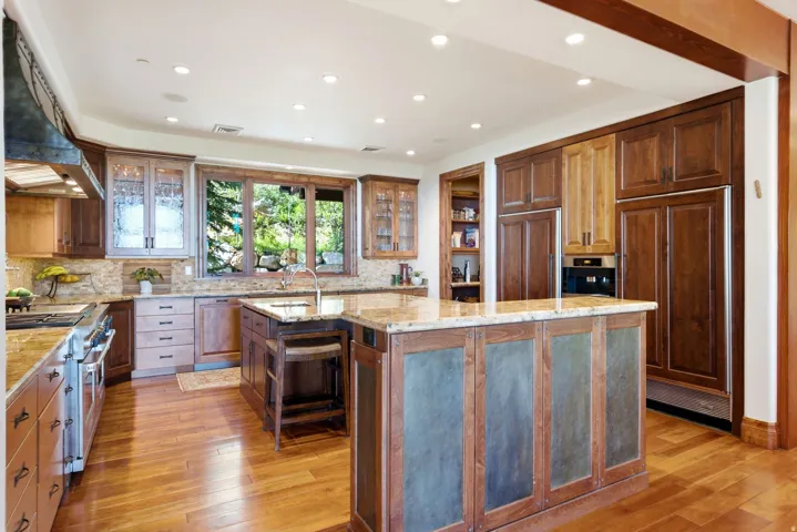 Spacious kitchen featuring a large central island with a stone countertop, wood-finish flooring, recessed lighting, custom cabinetry, and built-in stainless steel appliances