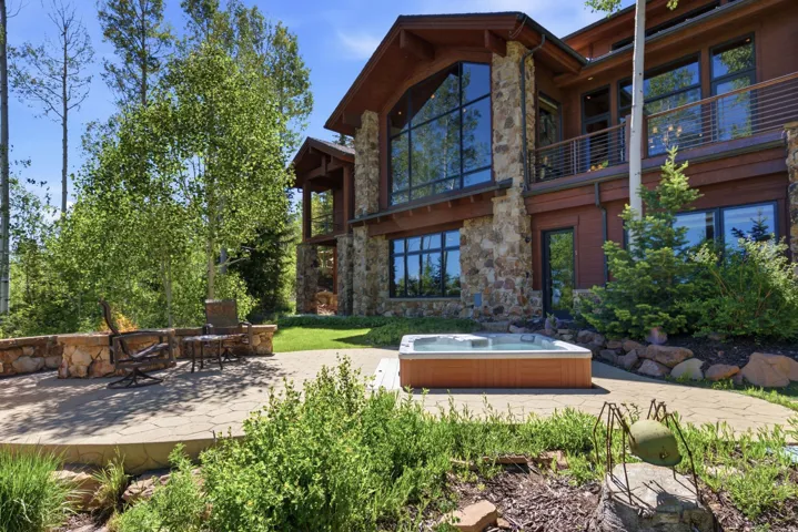 Expansive stone patio featuring a built-in hot tub, surrounded by mature trees and natural landscaping