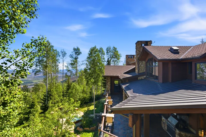 Multi-level residence featuring a brown shingle roof, stone chimneys, and dark-stained exterior siding