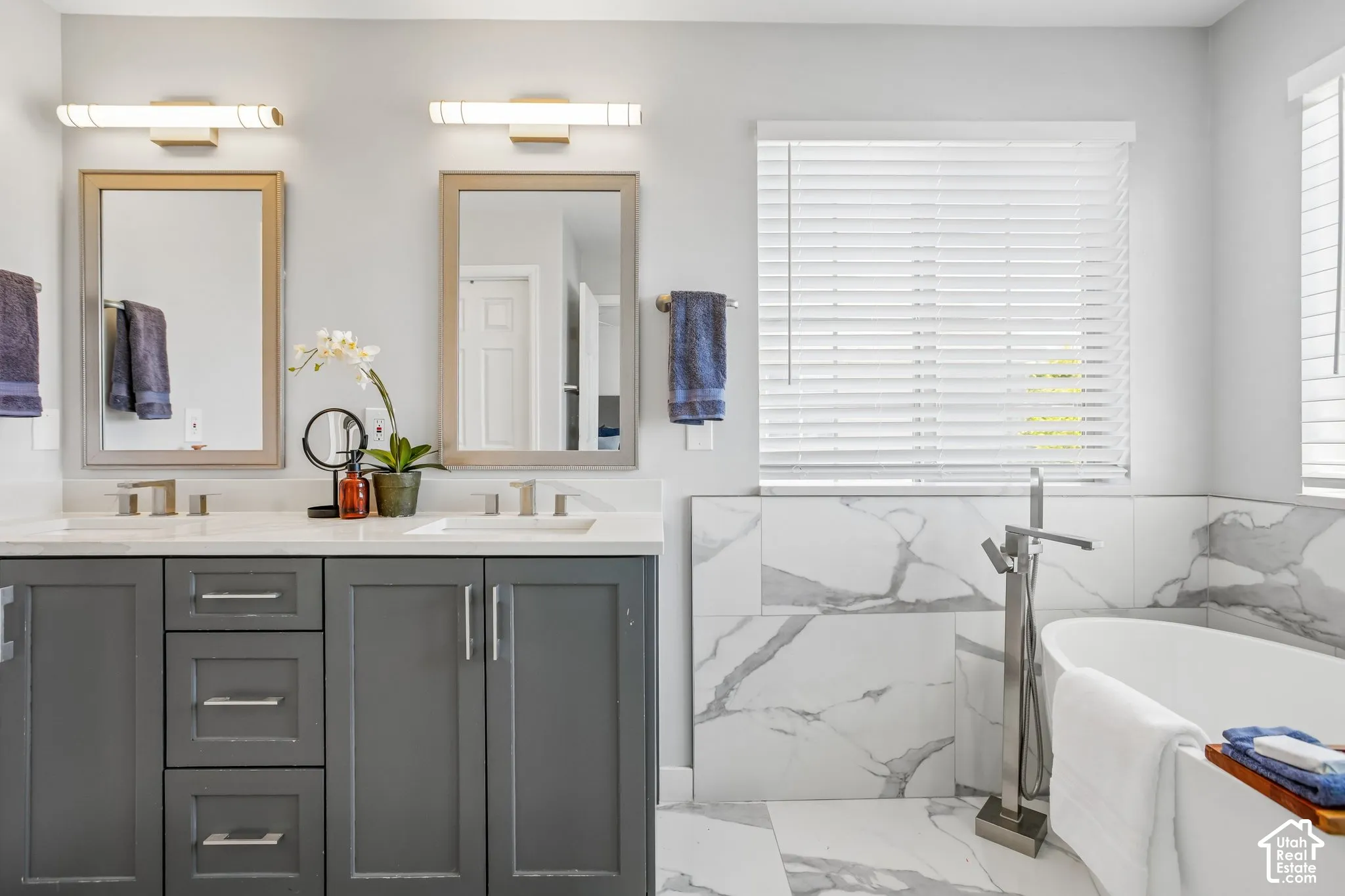 Bathroom featuring dual vanities with dark gray cabinetry and light-toned countertops