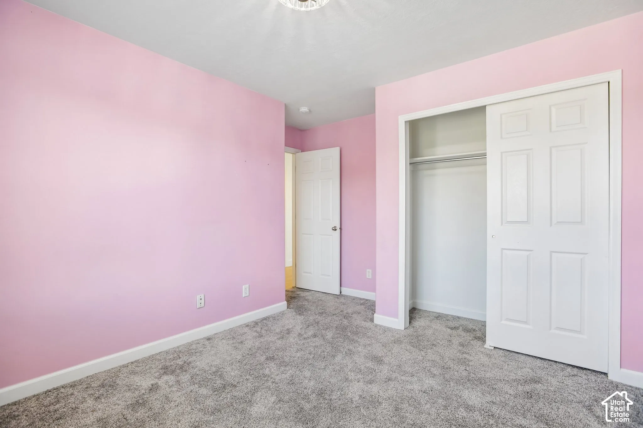 Room featuring soft pink walls, plush gray carpeting, and a white six-panel bi-fold closet door