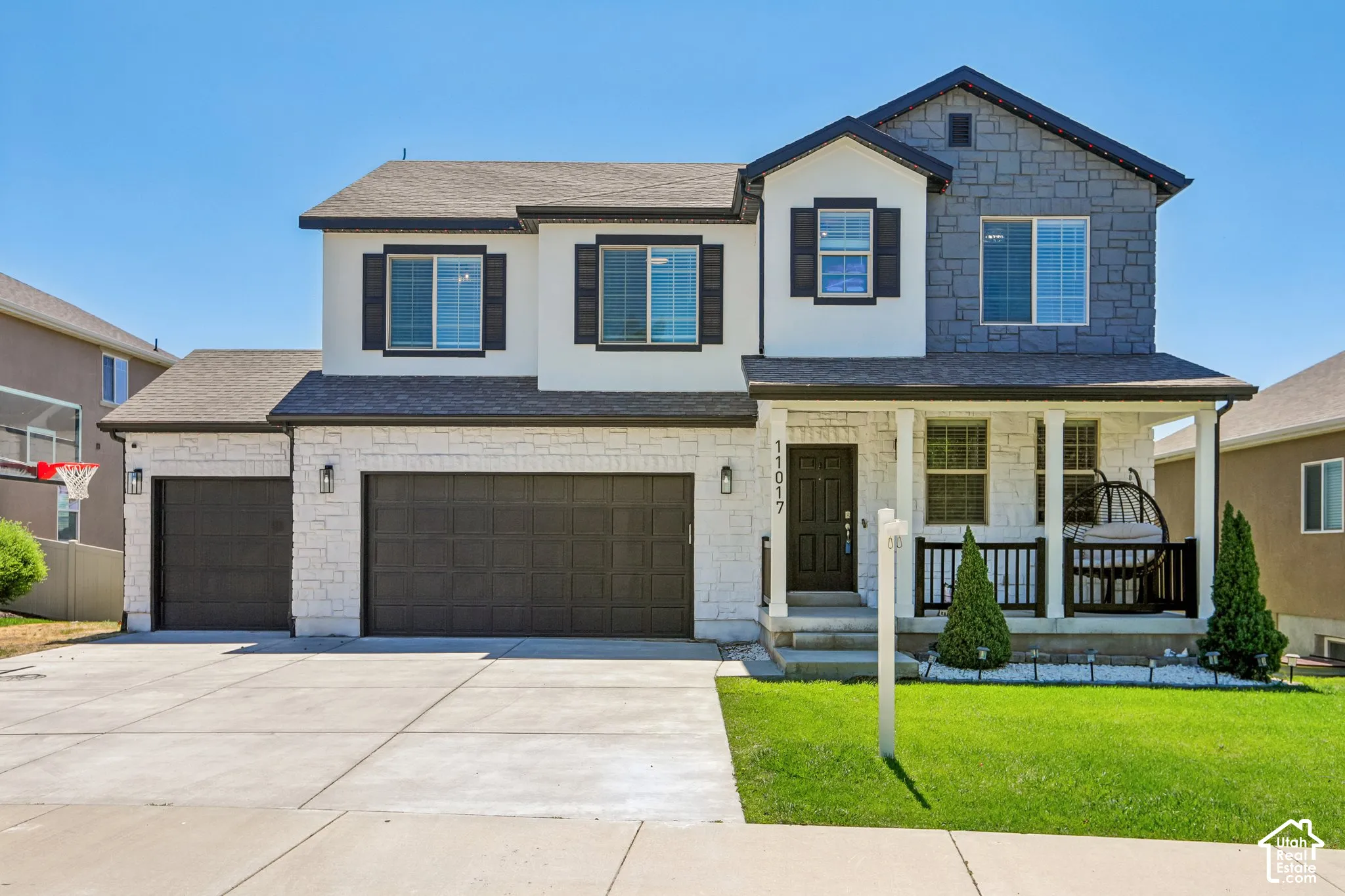 Contemporary two-story residence featuring a covered front porch, a mix of stone and stucco exterior finishes, and dark window shutters