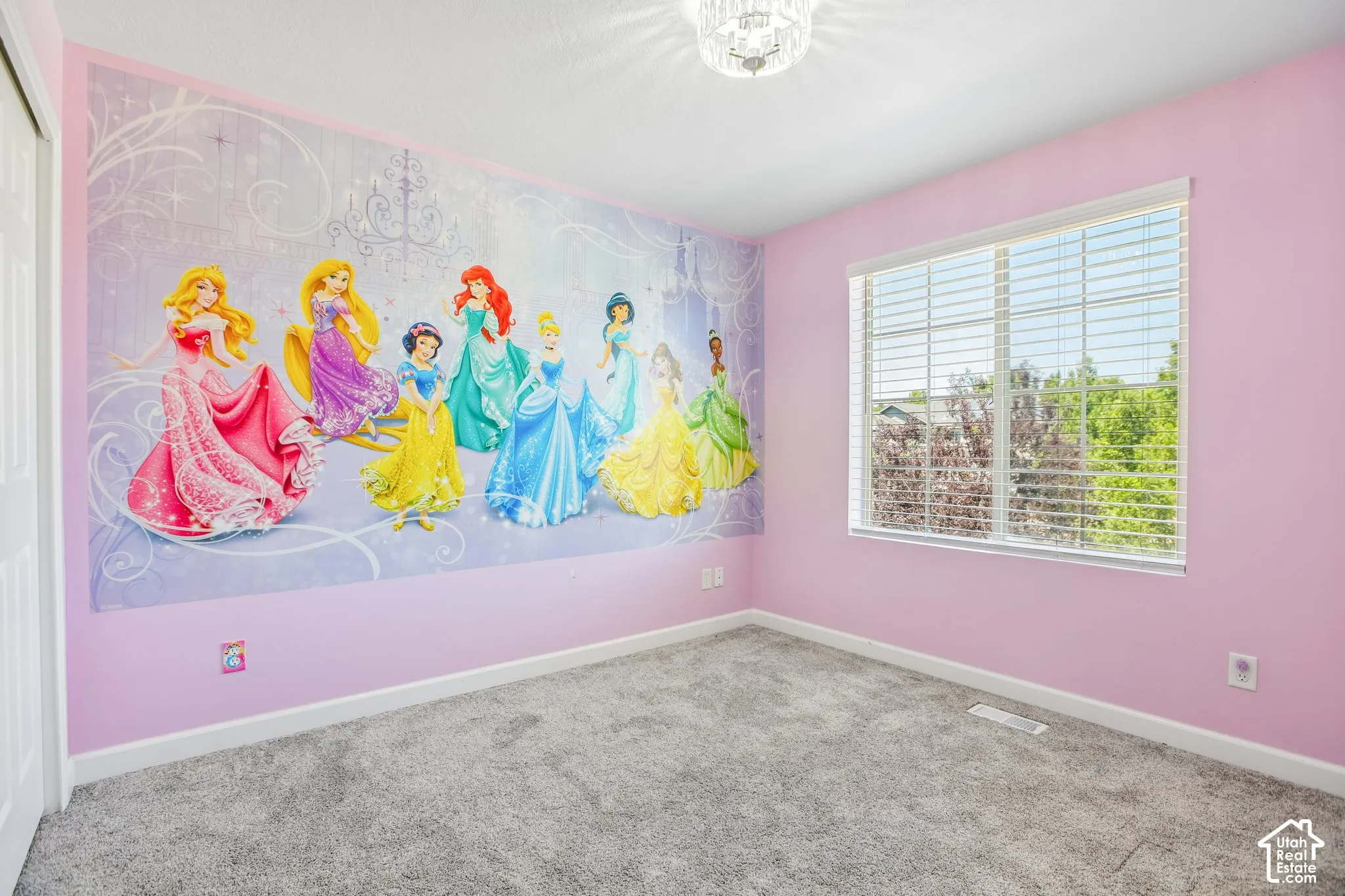 Spacious room featuring a decorative wall mural, plush grey carpeting, and a large window with white blinds