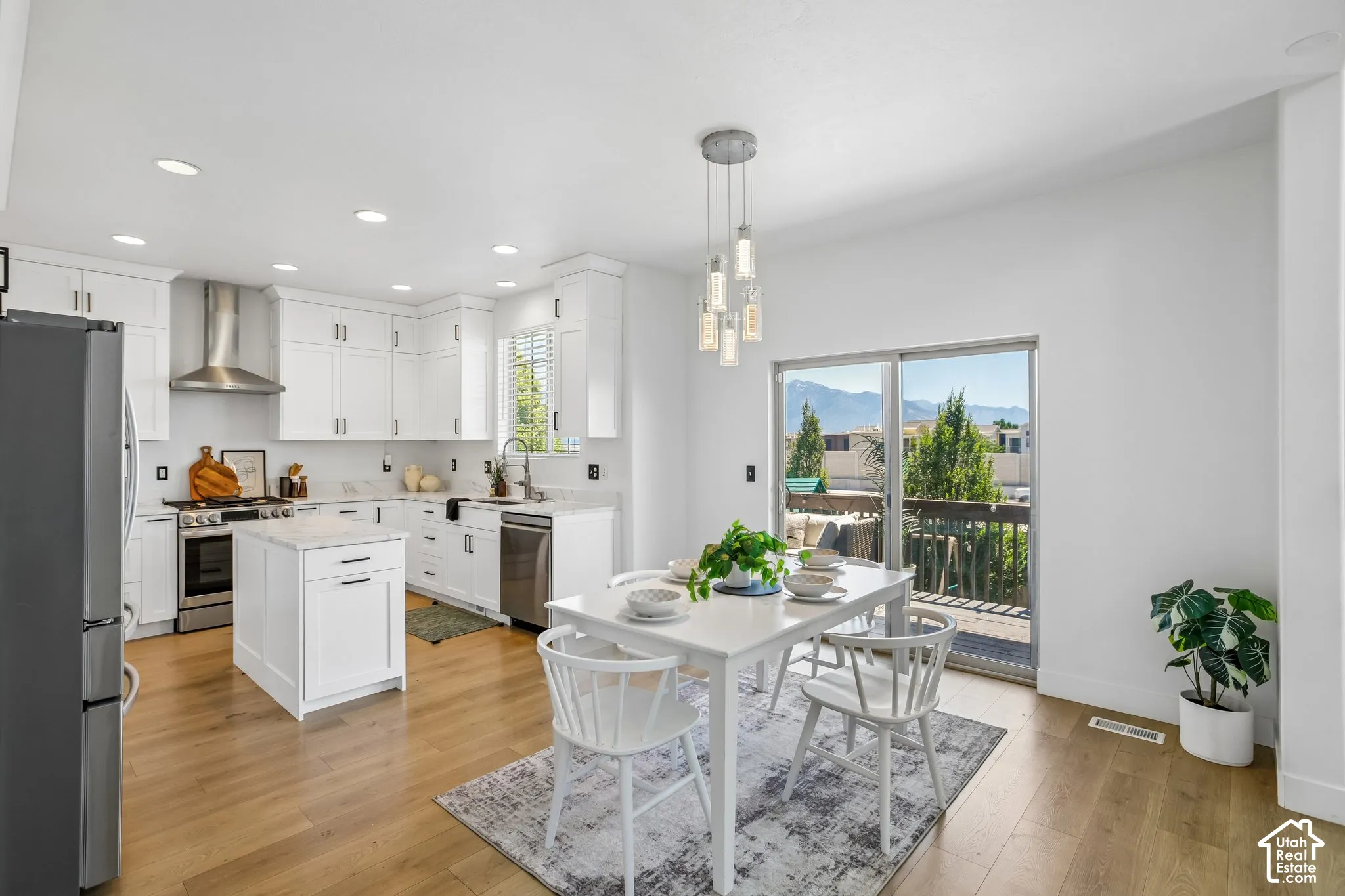 Bright open-concept kitchen and dining area featuring light wood-finish flooring, white cabinetry with black hardware, stainless steel appliances, and a central kitchen island