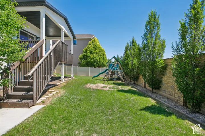 Expansive backyard featuring a manicured lawn, a concrete patio, and a covered wood deck with stairs