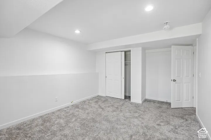 Spacious room featuring plush gray carpeting, recessed ceiling lighting, crisp white walls, and two white paneled doors