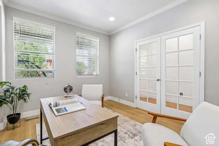 Bright interior space featuring light wood-finish flooring, dual windows with blinds, and white French doors with glass panels