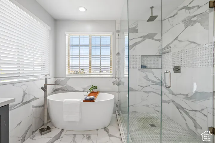 Freestanding soaking tub with a floor-mounted faucet, complemented by a large walk-in shower featuring a rain showerhead, glass enclosure, and patterned tile accents