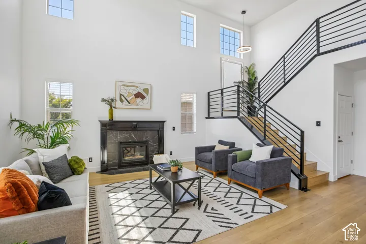 Two-story living area featuring high ceilings, a fireplace with a dark marble-style surround, wood-finish flooring, a contemporary staircase with black metal railings, and multiple windows