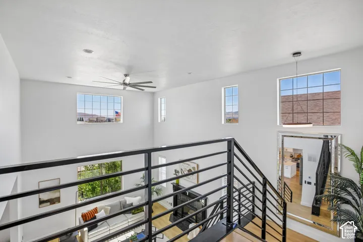 Multi-level interior featuring a contemporary black metal railing, a prominent ceiling fan, and a modern pendant light fixture