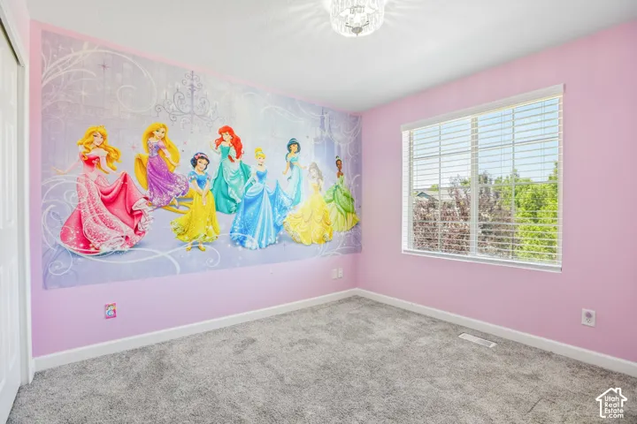 Spacious room featuring a decorative wall mural, plush grey carpeting, and a large window with white blinds