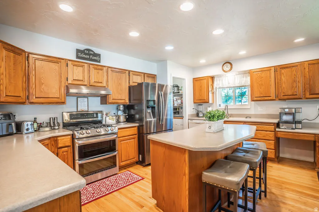 Kitchen featuring wood-finish cabinetry, stainless steel appliances, a center island with seating, and recessed lighting