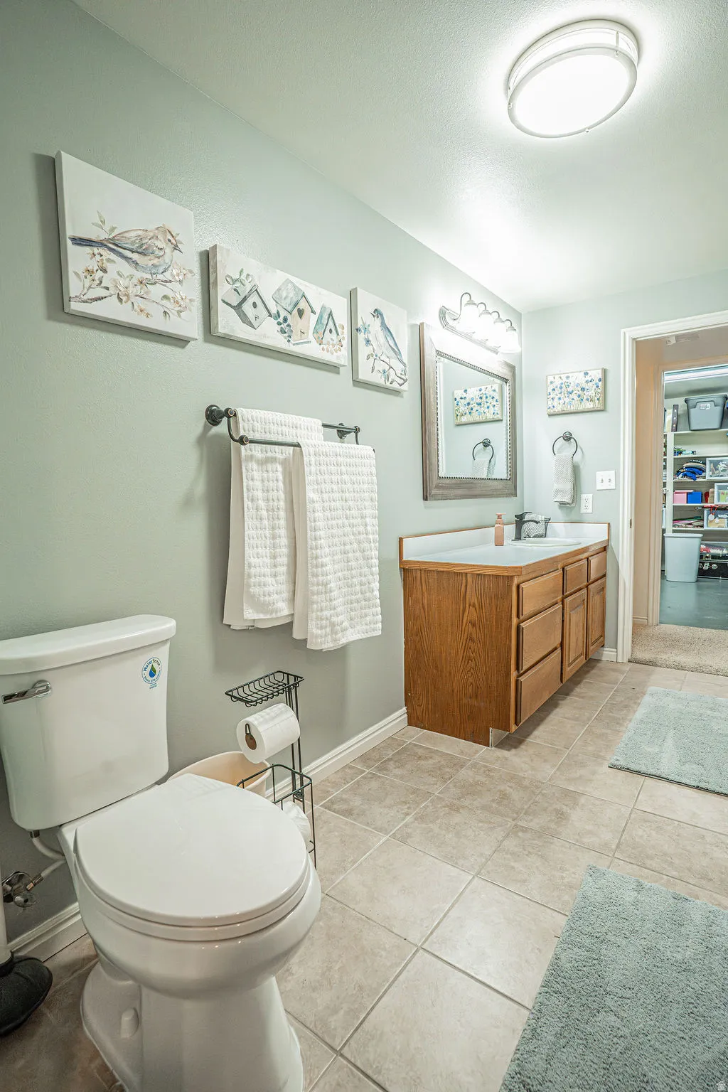 Bathroom featuring a wood-finish vanity with ample storage, tiled flooring, a contemporary ceiling light fixture, a wall-mounted mirror with integrated lighting, and a white toilet
