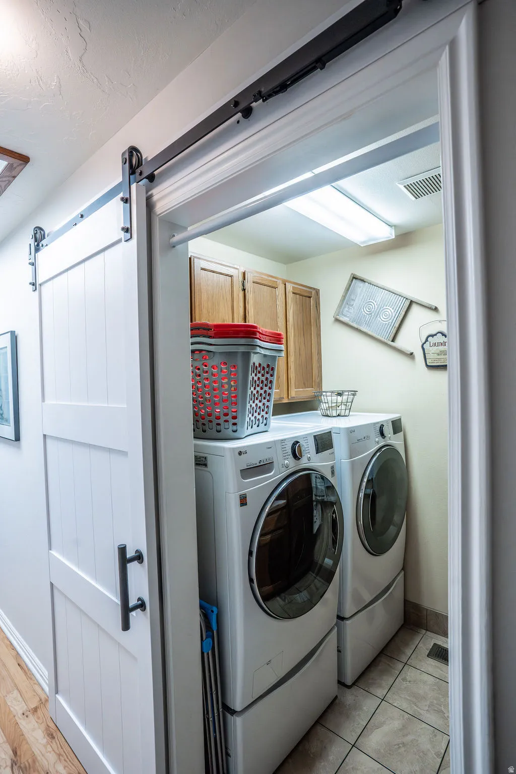 White barn door entry to a dedicated laundry space with overhead fluorescent lighting, wood-finish cabinetry, and tiled flooring
