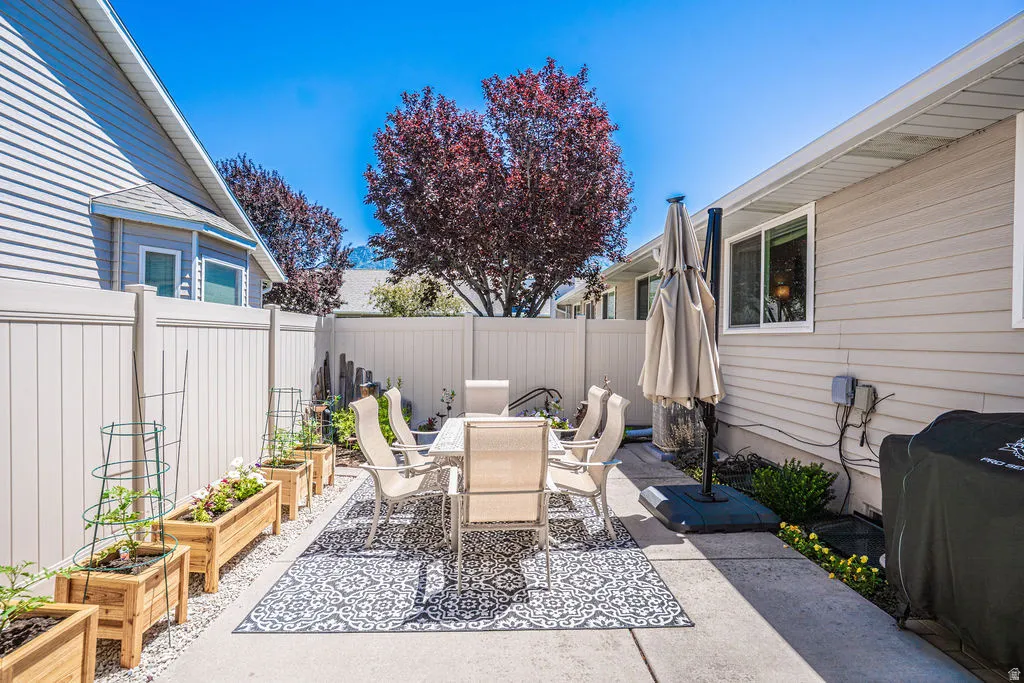 Paved patio area featuring privacy fencing, mature landscaping, and raised garden beds