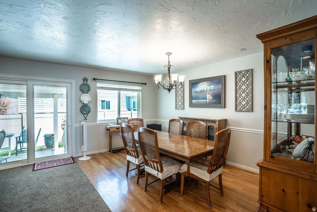 Dining area featuring warm wood-finish flooring, a contemporary chandelier, chair rail molding, and an expansive window with blinds