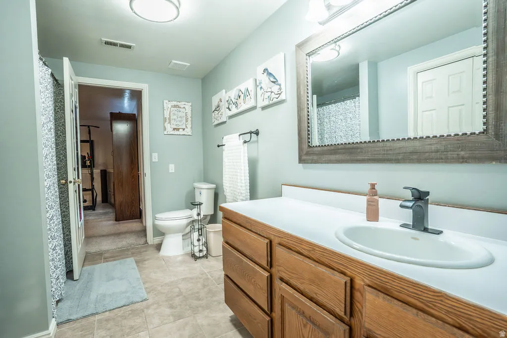 Bathroom featuring a wood-finish vanity with a white countertop and integrated sink, a rectangular framed mirror, and tile-finish flooring