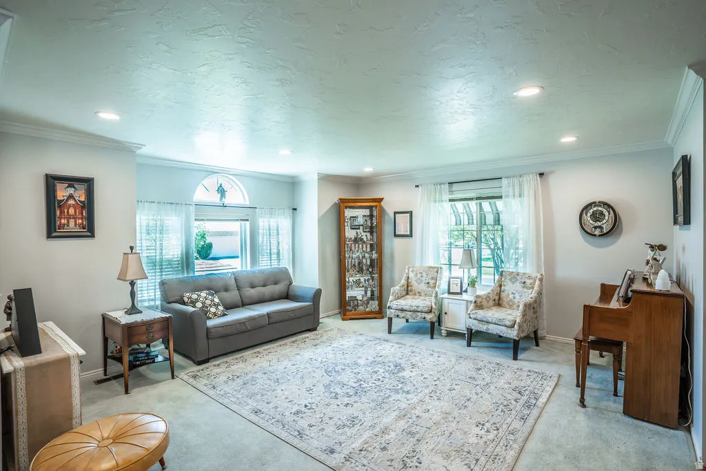 Recessed lighting illuminates this living space featuring light gray walls, white crown molding, and light-colored carpeting