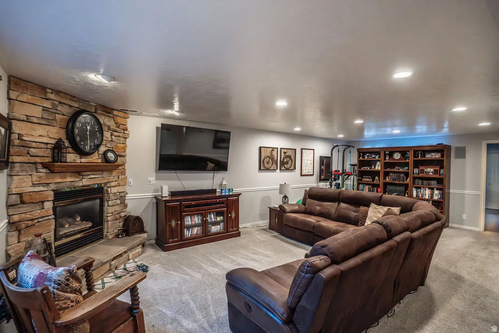 Finished basement featuring a stone fireplace with a wood mantle and hearth, recessed lighting, carpet flooring, wainscoting, and built-in shelving