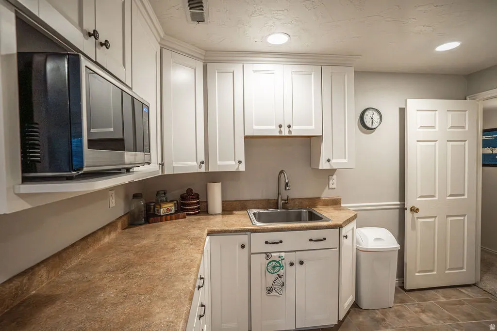 Kitchenette featuring white cabinetry, integrated microwave, stainless steel sink with gooseneck faucet, and mottled brown countertops
