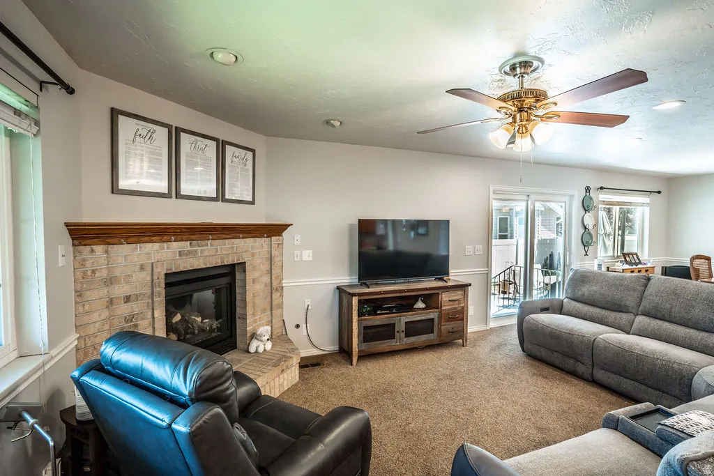 Living area featuring a brick-surround fireplace with a wood mantel, overhead ceiling fan with light fixture, recessed lighting, and carpet flooring