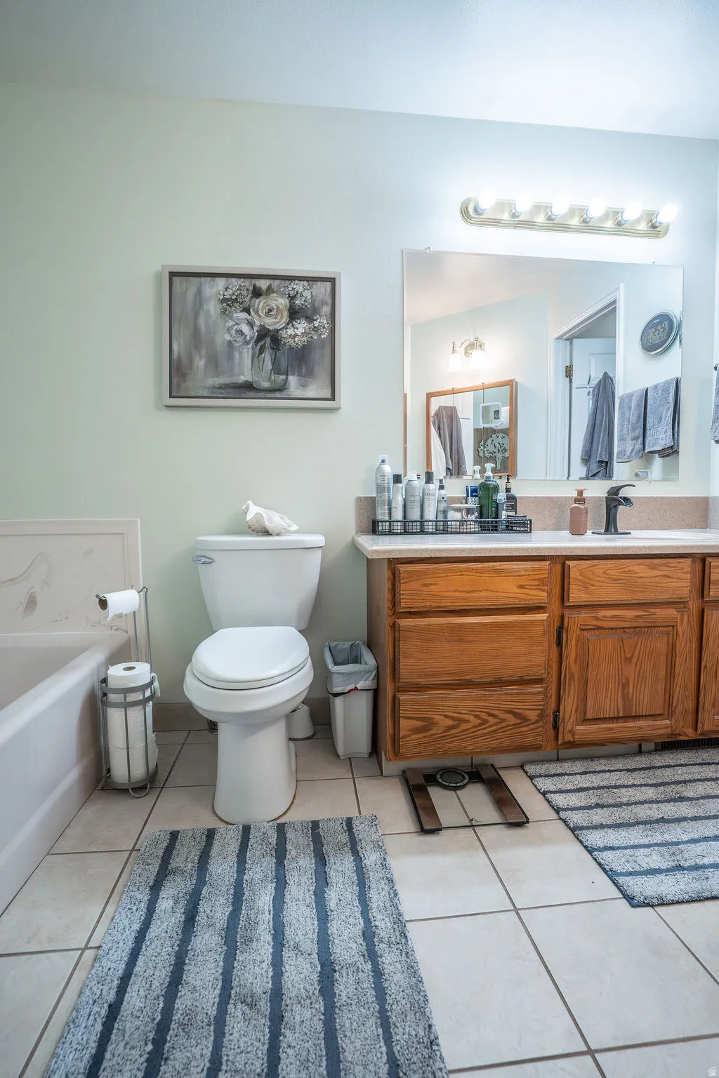 Bathroom featuring a wood-finish vanity with a light-toned countertop, a mounted mirror, and a multi-bulb light fixture
