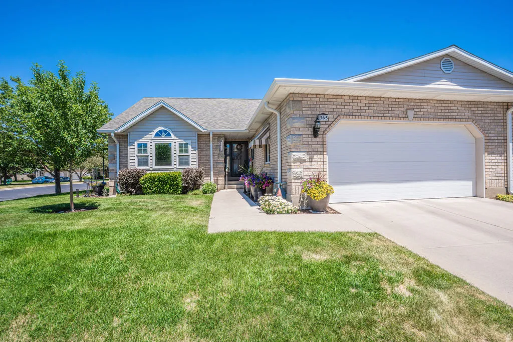 Brick and siding exterior featuring a two-car garage with a concrete driveway, a gabled roof, and a mature tree in the front yard